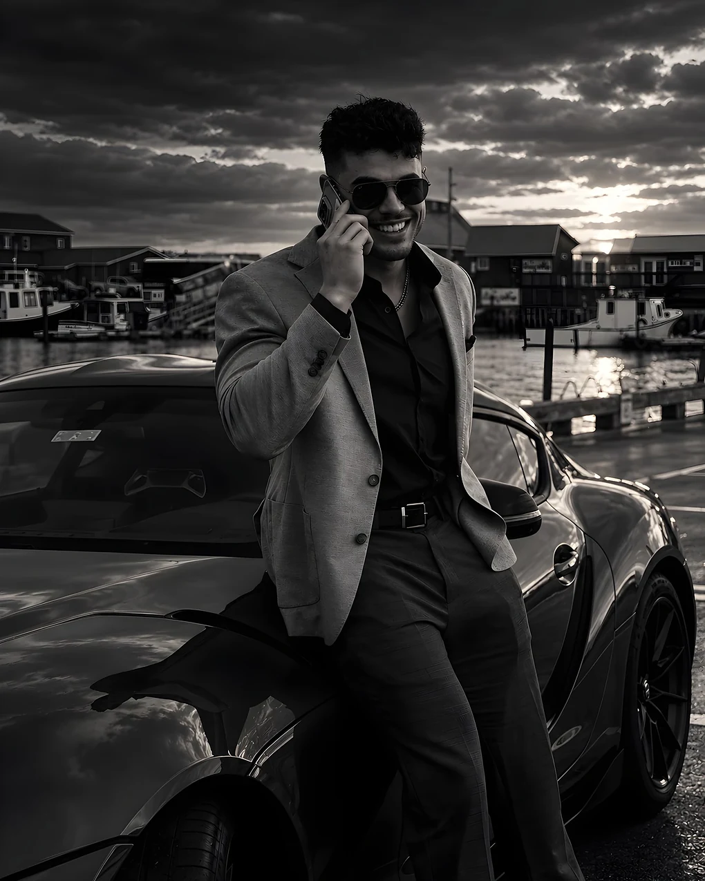 Phil Dave on a phone call, leaning on a car by the harbour at dusk